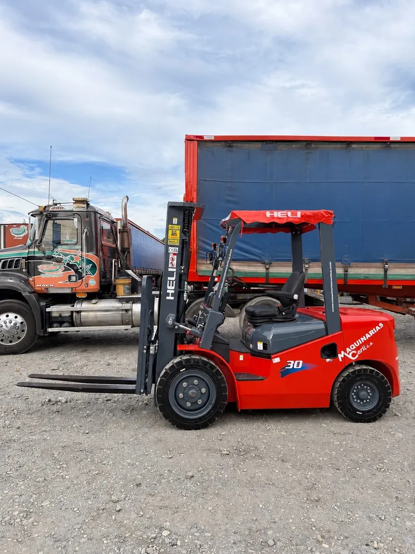 Montacargas Heli de 3 toneladas, nuevo, rotulado con la marca y la web de Maquinarias Carli, en un patio junto al camión de transporte.